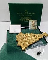 Brass Christmas trivet with holly motif resting in foam insert inside original Virginia Metalcrafters box, accompanying informational cards and bagged screws visible