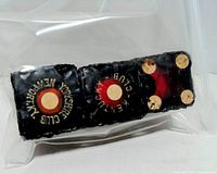 Three black wooden dice in plastic bag, top faces showing red centers with brass-tone stamped rings
