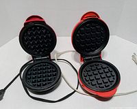 Both waffle makers open showing interior grids and cords
