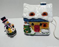 Front view of snowman trinket box beside lighted ceramic house