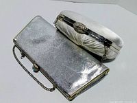 Silver metallic clutch and white ruched clutch side by side, showing exterior surfaces and clasps