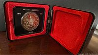 British Columbia 1871-1971 silver dollar coin mounted in black holder inside open presentation case with red velvet interior.
