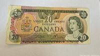 Front of 1979 Canadian $20 bill showing Queen Elizabeth II portrait and coat of arms with denomination.