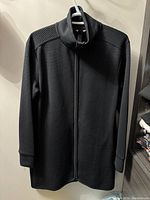 Front view of black ribbed full zip jacket with high neck and visible pocket openings and full length zipper
