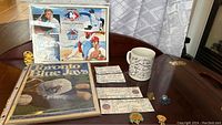 Framed print featuring Blue Jays players and logo, magazine, ticket stubs, coffee mug, and pins arranged on wooden surface.