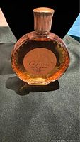 Photo of front of clear glass bottle labeled 'Capricci Eau de Toilette' with amber liquid inside, placed on dark fabric.