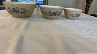 Set of three vintage Pyrex nesting bowls displayed side by side, increasing in size from right to left showing the classic Homestead blue floral pattern on tan granite background.