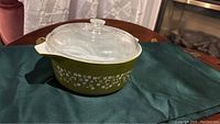 Front angled view of avocado green Pyrex deep casserole with glass lid, showing floral pattern and overall condition.