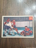 Front image of 1954 Parkhurst #98 Plante hockey card showing hockey players in action, Plante protecting against Sloan, card number 98 in top right corner.
