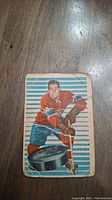 Front view of the hockey card with player in red jersey and blue shorts posing with hockey stick and puck.