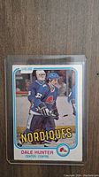 Front of Dale Hunter rookie hockey card showing player in Quebec Nordiques blue jersey with goalie and other players in background. Card labeled O-Pee-Chee, with player name and position.