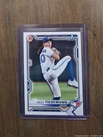 Front view of Ricky Tiedemann Bowman First Rookie Baseball Card in protective sleeve on wooden surface.