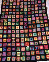 Full view of the crocheted granny square afghan showing multiple colorful squares with black background.