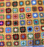 Close-up photo showing crocheted granny square afghan blanket with gold background and multicolored squares