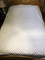 Full view of the white bedspread laid out over a wooden bed frame, showing the textured diamond pattern.