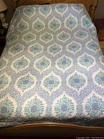Full view of bedspread laid out on a bed showing repeating ornate blue and green patterns on a white background.