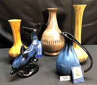 Five Blue Mountain Pottery pieces including two Harvest Gold vases, one Mocha glaze vase, one Cobalt blue pottery bird figurine, and one cobalt blue pitcher with handle set against a black background.