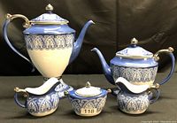 Front view of complete Bombay tea and coffee service set showing 10-inch coffee pot, 6-inch tea pot, two creamers, and sugar bowl in blue, white, and gold pattern.