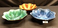 Photo of three Blue Mountain Pottery bowls in green, harvest gold, and blue colors displayed together on a black surface.