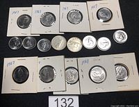 Overall view of 15 Canadian 5-cent nickels and 2 quarters from 1967 arranged flat, some in cardboard holders.