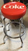 Full view of Coca Cola bar stool showing red cushioned seat with white Coke logo and chrome legs