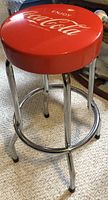Side view of the red Coca Cola bar stool showing the chrome legs and footrest.