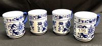 Four white ceramic tea cups with blue floral and vine patterns arranged in a row, each with a handle.