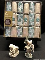 Photo of the box containing 12 festive Christmas crackers with polar bear print and silver glitter designs, plus two Christmas figurine ornaments placed in front of the box.