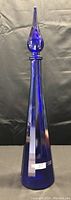 Full view of tall blue genie bottle with pointed stopper on black background