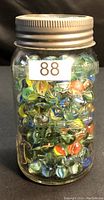 Glass jar filled with assorted marbles, sealed with metal lid, labelled with "88"