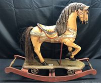 Side view of antique wooden rocking horse with carved mane and tail on rocker with wheels