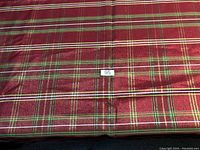 Photo shows the full cloth surface with a red plaid pattern incorporating green, white, and yellow stripes, and a sticker tagged with '95'.