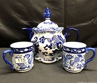 Front view of the blue and white ceramic teapot and two matching cups showing floral pattern and overall condition