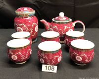 Photo of the entire 8 piece oriental tea set showing teapot, tea cannister, and six matching teacups with red and gold decorative patterns.