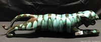 Green and black pottery tiger figurine laying down with head turned slightly, showing body stripes and glossy finish.