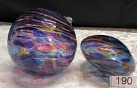 Photo of two hand blown glass balls on a table, one large and one medium, both with colorful swirling patterns inside.