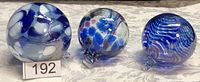 Photo of three hand blown glass witch's balls featuring unique multi-colored patterns in blue, white, and purple tones.