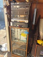 Stack of Sharp audio equipments including receiver, tape decks, and equalizer inside a wooden cabinet with glass door