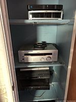 Shelves with stacked audio and media devices: silver Onkyo receiver, Philips Digital Stream DVD, black JVC VHS player, Blu-ray player, and another black device.
