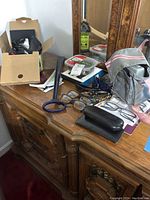 Photo showing mini video camera, reading eyeglasses, eyeglass cases, and a carrying bag on a wooden dresser surface.