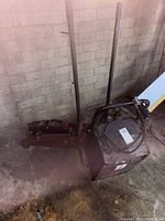 Black car battery charger and two hydraulic floor jacks placed against a brick wall on a concrete floor.