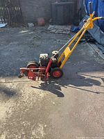 Side view of McLaren gasoline hedge trimmer showing yellow handle and red blades on concrete outdoor surface.