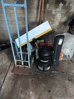 Blue hand truck dolly alongside vintage Remington space heater, black insect catcher, and metal reflector. Electrical cords coiled.
