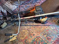 Full view of three gas-powered hedge trimmers lying on a rug showing shafts, handles, and engines
