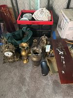 Wide view showing plastic crate with plates, glass vases, brass items including clock, vases, figurines and eyeglass case