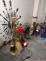 Wide view showing brass fireplace tools, metal starburst wall art, Christmas plush decorations, glass vases and other decor items on the floor and against wall.