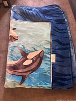 Folded ocean-themed throw blanket showing whale and blue tiger-striped edges.