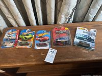 Five unopened Hot Wheels cars in original packaging displayed on a table with curtains in background.