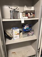 Shelf with kitchen scale, Black & Decker chopper box, boxed toaster oven, and other kitchen appliances and tools.