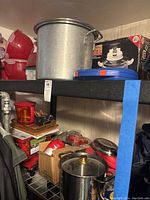 Photo showing large aluminum pot, boxed gourmet air fryer, and various plastic containers and small cookware on shelving.
